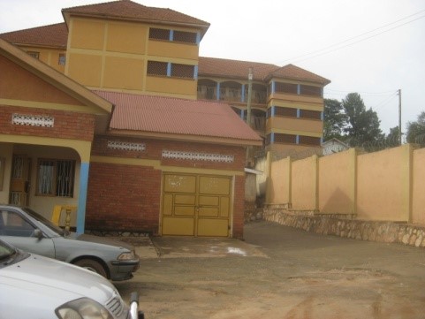 A school building with yellow and orange roof and walls. Two cars are in the car park.