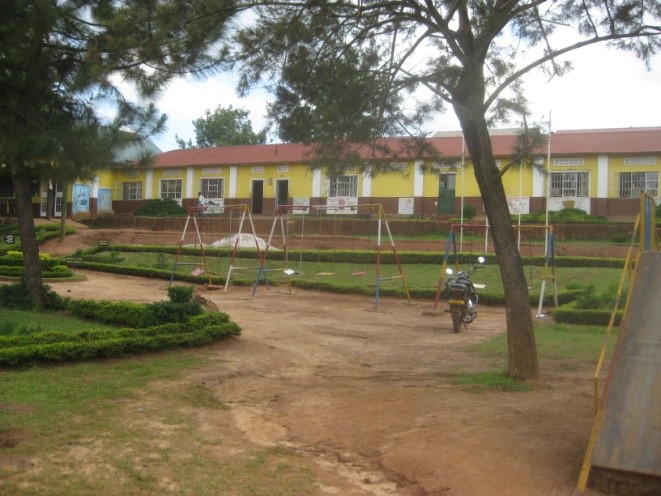 A school building with yellow walls and a red roof. Play equipment is in the foreground.