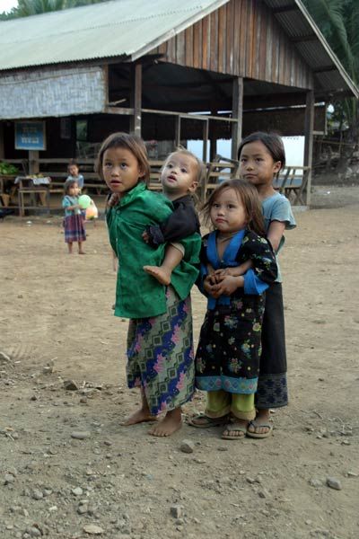 Three children stand together, the child on the left is carrying a fourth child.