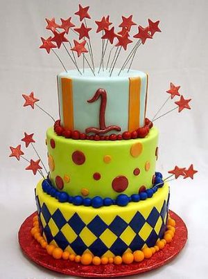 A birthday cake with three layers, there's a big 1 on the top layer. There are stars on thin wires stuck into the cake.