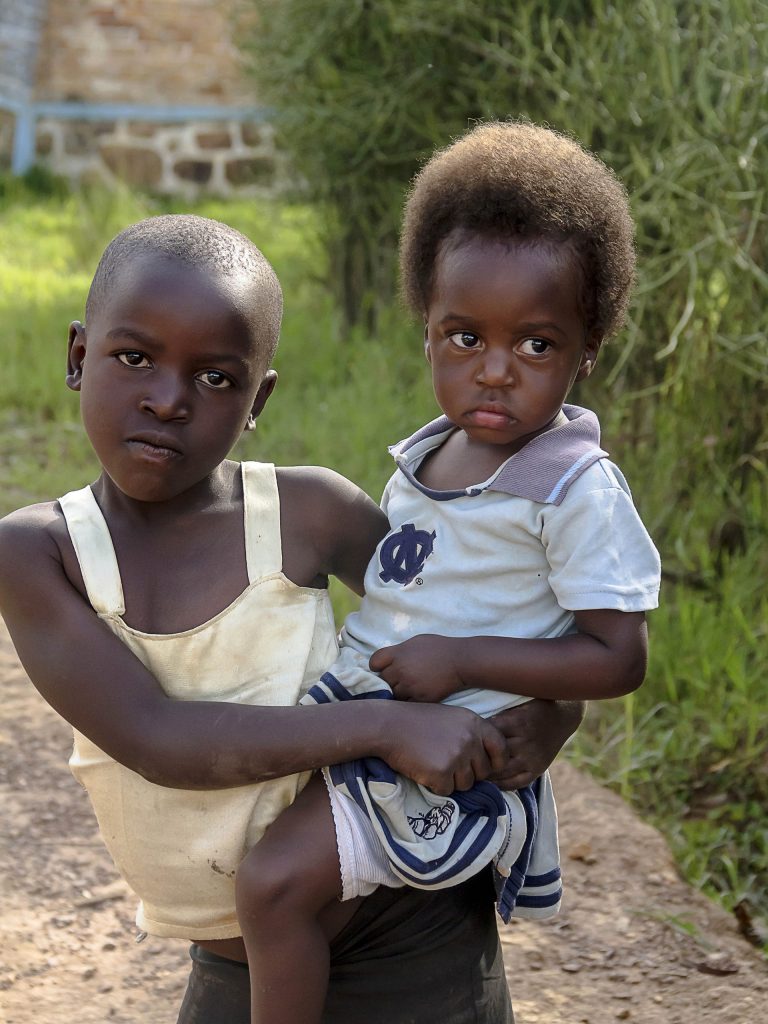 A photo of an older child in a white strappy tip is holding a toddler on their hip.