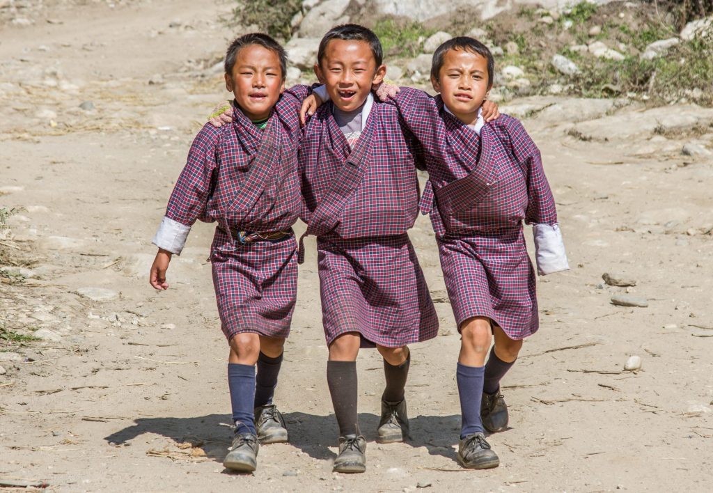 Three children walking together in blue and red robes. The centre child has black socks and the other two have blue.