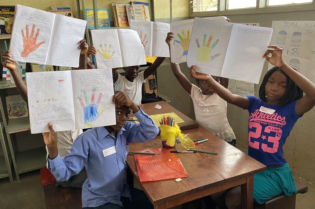 A group of children hold up their notebooks with their work so far.