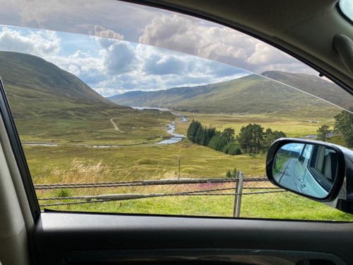 Photo taken from a car window of some hills and a river in the highlands of Scotland