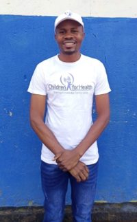 Kelvin smiles at the camera, he is wearing a Children for Health t-shirt and jeans.